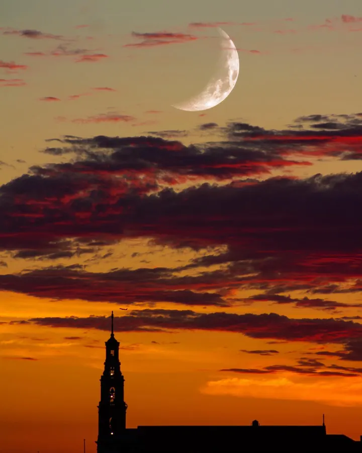 Crescent moon over a steeple at sunset