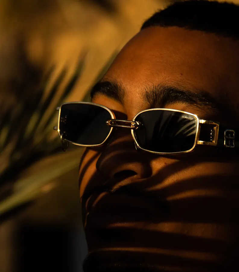 Close portrait of a man in gold sunglasses with palm shadows across his face