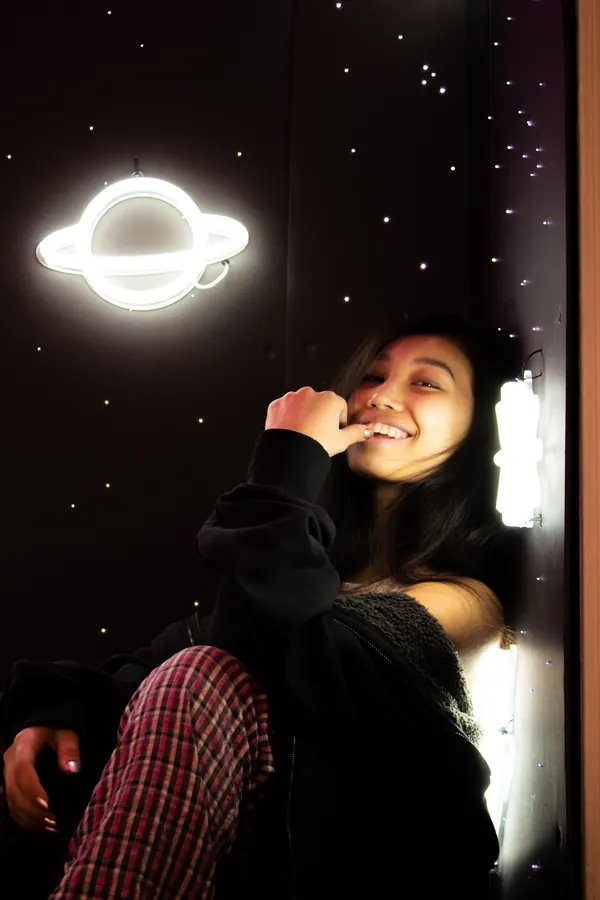 Woman smiling beside a neon planet sign