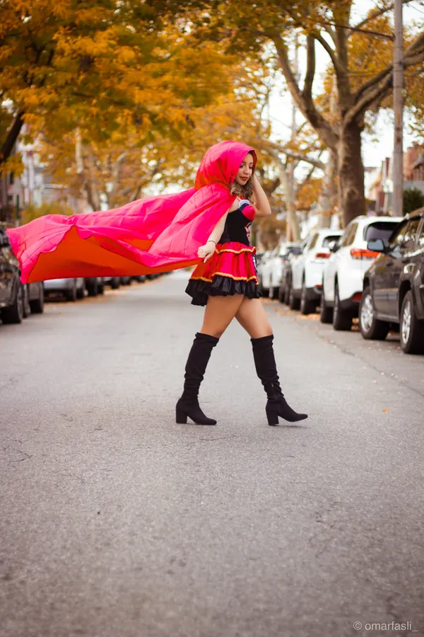Red Riding Hood costume with the cape blowing on a tree-lined street