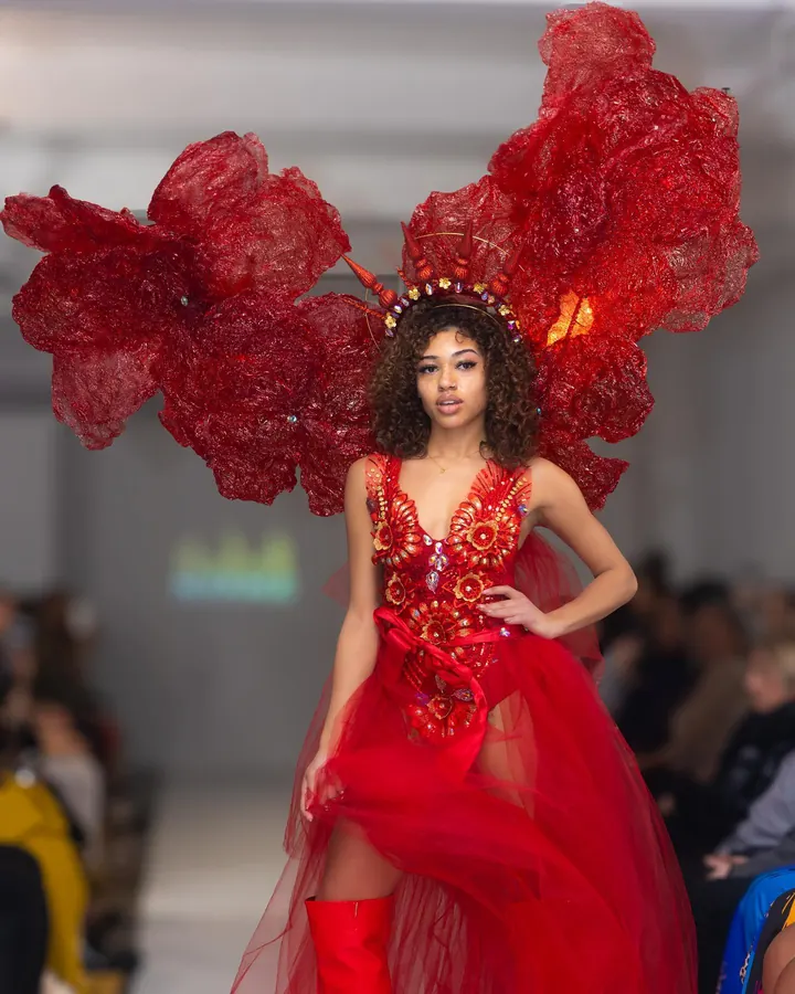 Model in a red dress with large red wings on the runway