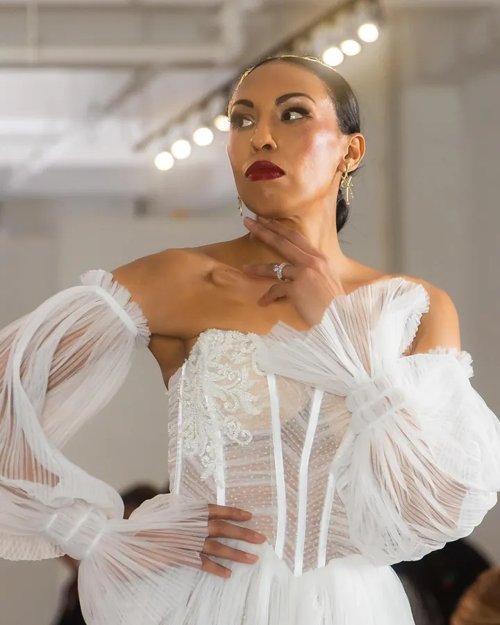 Model in a white corset gown with sheer sleeves on the runway