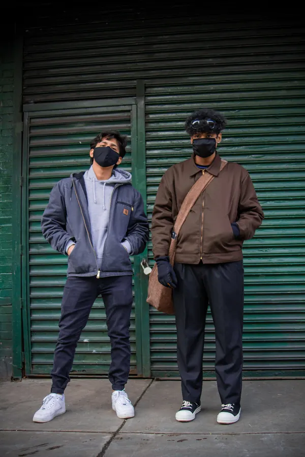 Two men in masks standing against a green shutter
